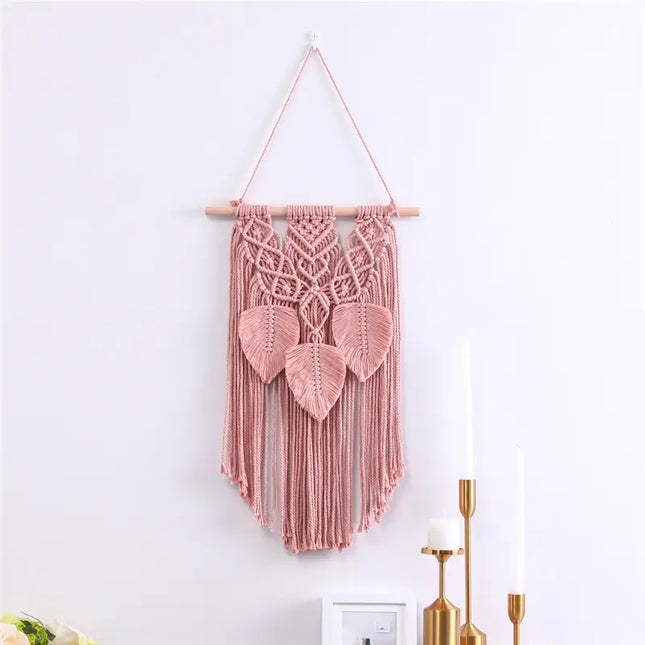 Pink macrame wall hanging with leaf design on a white wall.