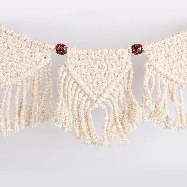 Macrame wall hanging with beige ropes and red beads on a light gray background