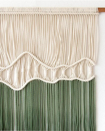 Macrame wall hanging with white top and green bottom on a white background