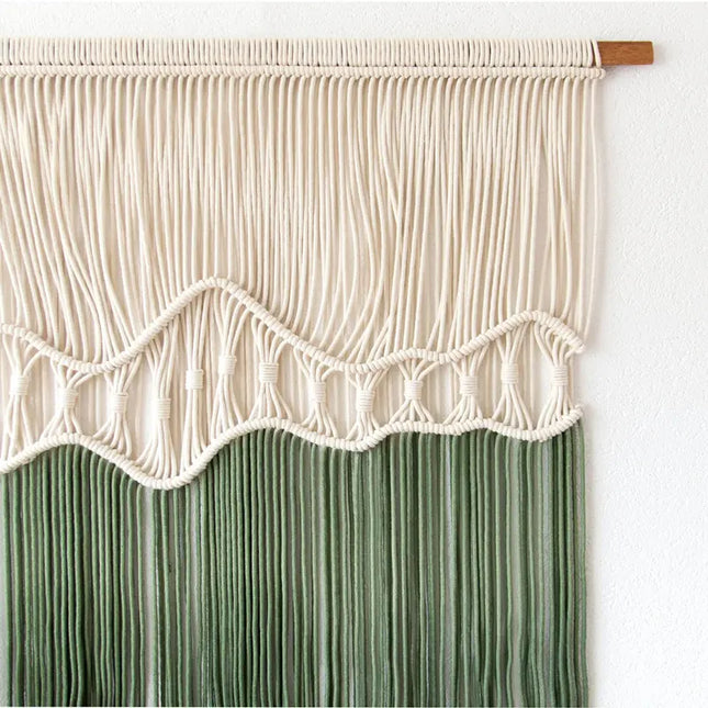 Macrame wall hanging with white top and green bottom on a white background
