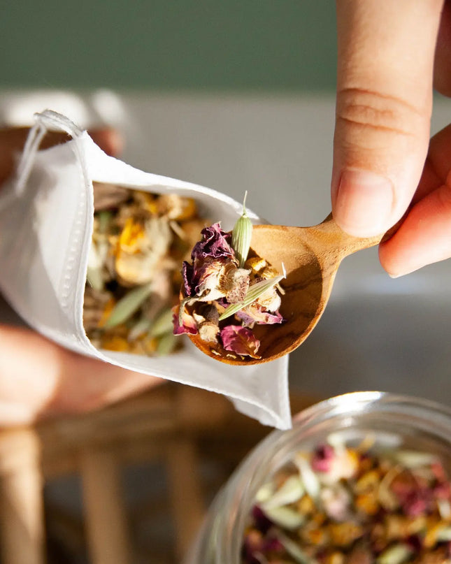 Filling compostable tea bag with Herbal Bath Tea blend using a wooden spoon"