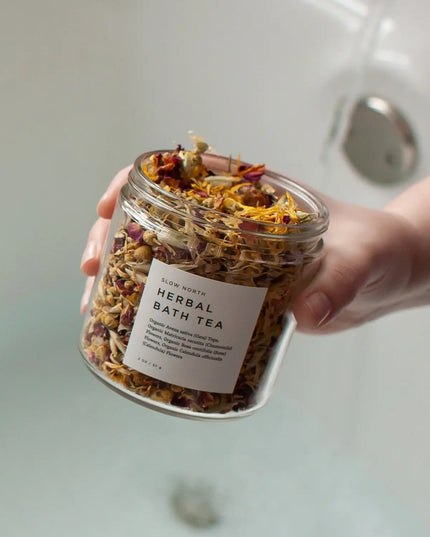 Herbal Bath Tea by Slow North – glass jar held by hand with bathtub in background