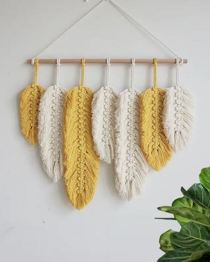 Woven wall art with yellow and white feathers hanging on a white wall.