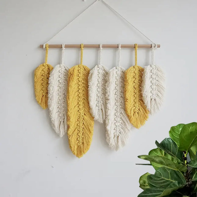 Woven wall art with yellow and white feathers hanging on a white wall.
