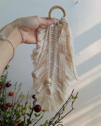 Hand holding a beige macrame wall hanging against a light background