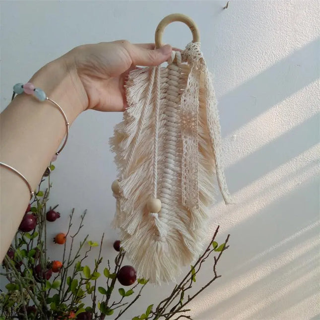 Hand holding a beige macrame wall hanging against a light background