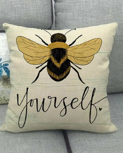 Pillow with a bee design and 'Be Yourself' text on a couch.