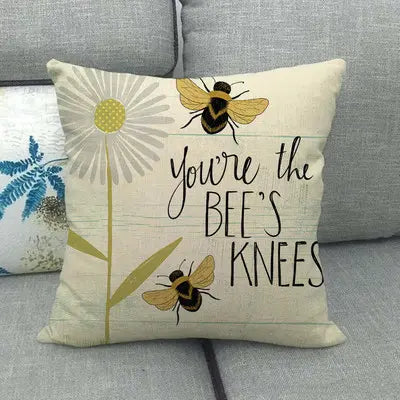 Decorative pillow with bee design and text 'You're the bee's knees' on a gray couch.