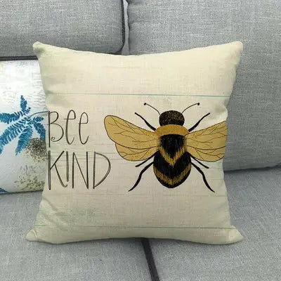 Pillow with a bee illustration and 'Bee Kind' text on a gray couch.