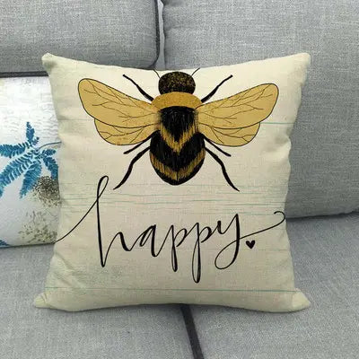 Decorative pillow with a bee illustration and the word 'happy' on a gray couch.