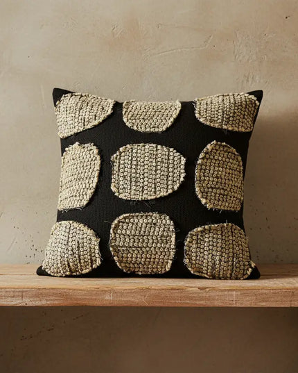 Decorative pillow with a geometric pattern on a wooden bench against a beige wall.