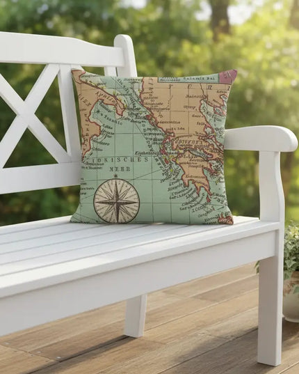 Map-patterned pillow on a white outdoor bench with a blurred green landscape in the background