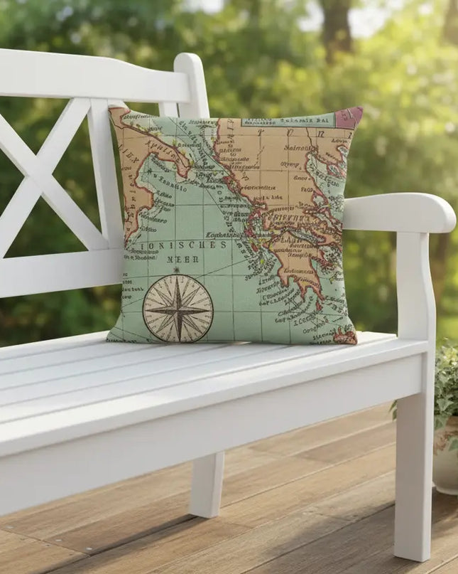 Map-patterned pillow on a white outdoor bench with a blurred green landscape in the background