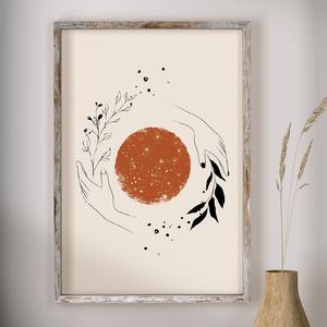 Framed artwork with a stylized sun and hands on a beige background, displayed on a wall.