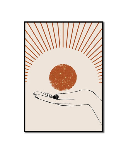 Framed artwork of a hand holding a small object with a sunburst design on a beige background
