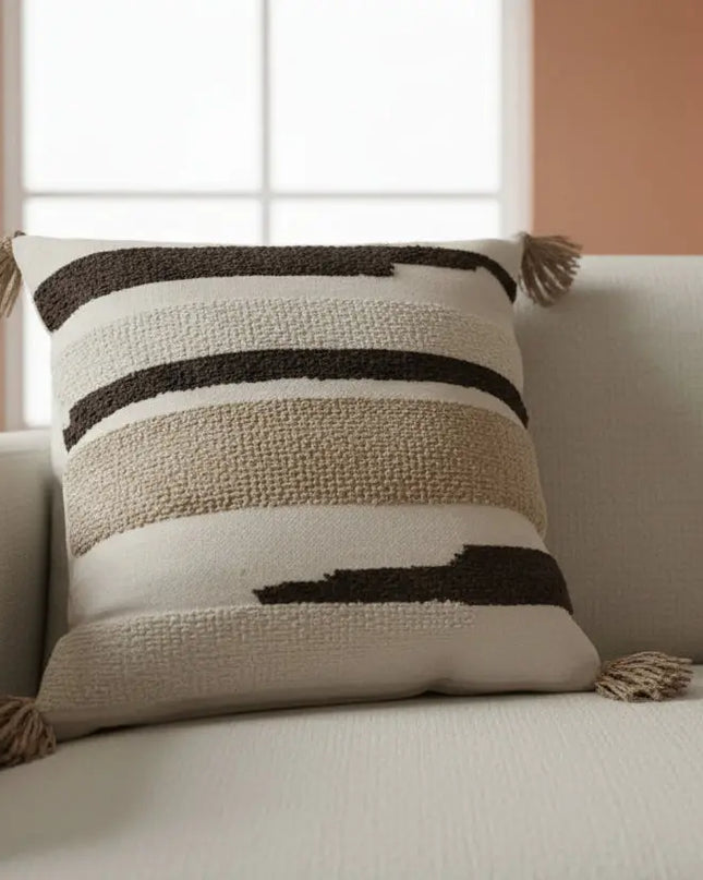 Textured pillow with black stripes and tassels on a beige sofa.