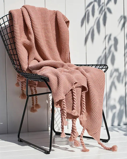 Pink knitted blanket draped over a black metal chair against a white wooden wall.