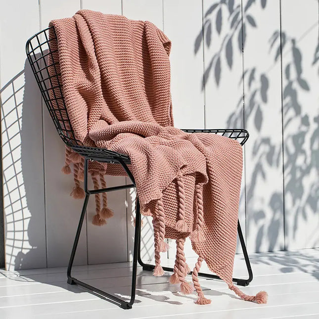 Pink knitted blanket draped over a black metal chair against a white wooden wall.
