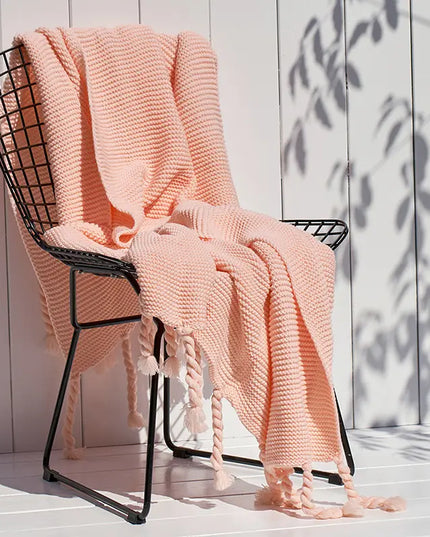 Pink knitted blanket draped over a black wire chair against a light wooden panel background