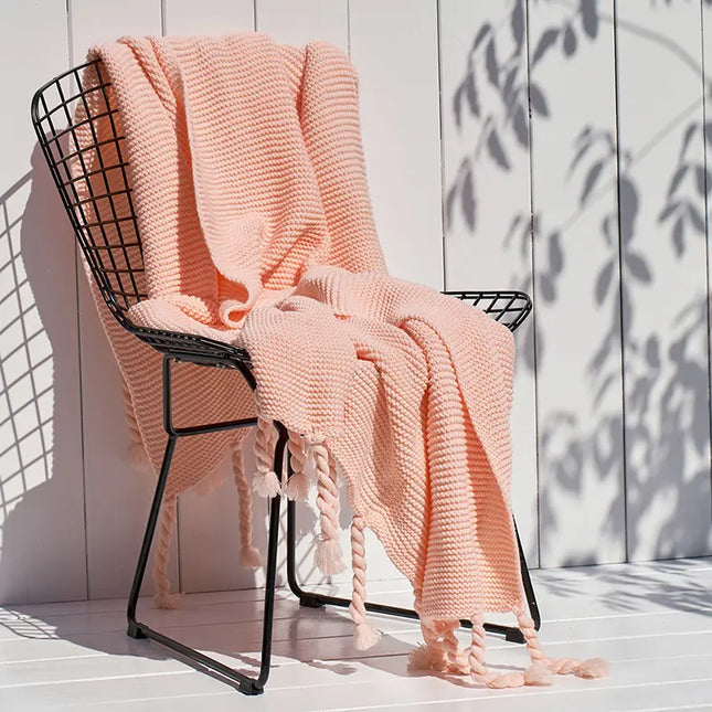 Pink knitted blanket draped over a black wire chair against a light wooden panel background