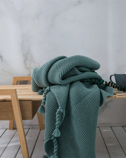 Ocean green knitted blanket draped over a wooden chair against a marble wall.
