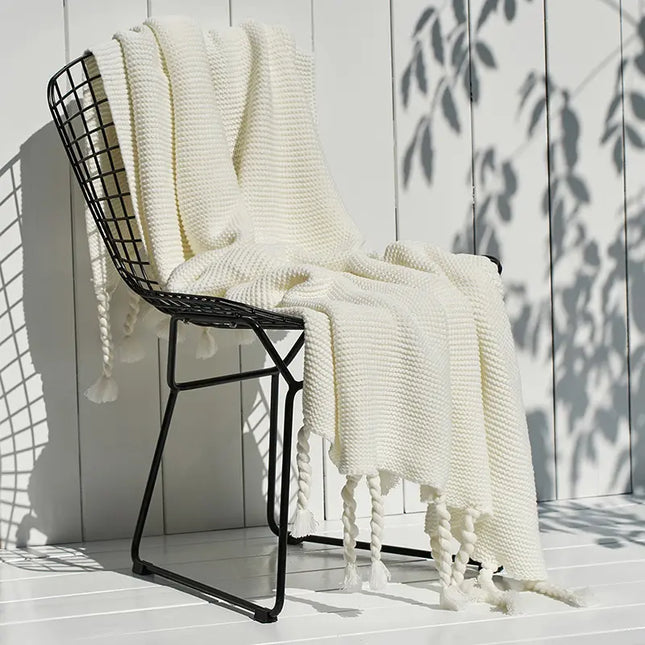 Black wire chair with a white knit blanket draped over it against a light wooden wall.