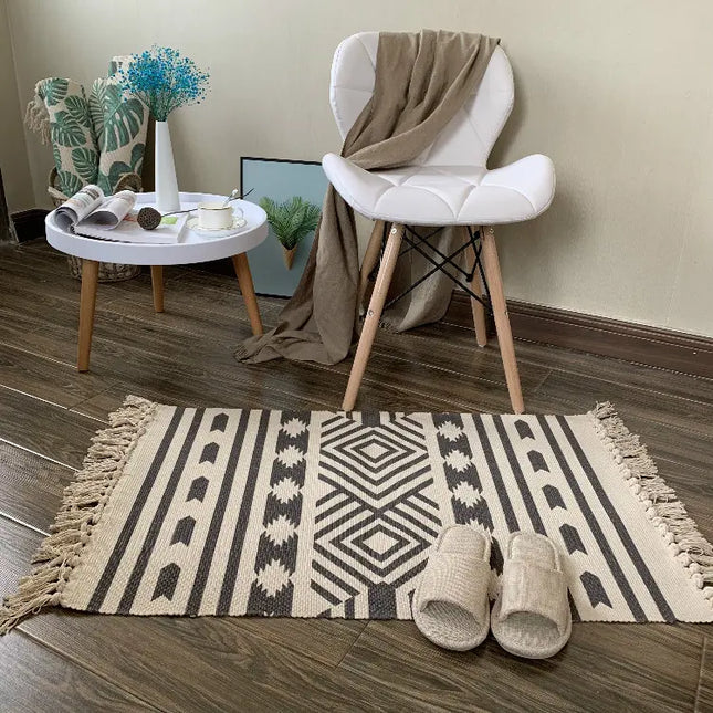 Patterned rug with slippers on a wooden floor, white chair with brown blanket, and small round table with decor items.