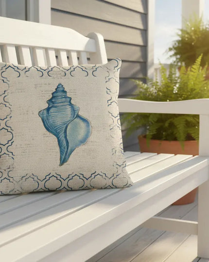 Decorative pillow with a blue shell design on a white bench outdoors.