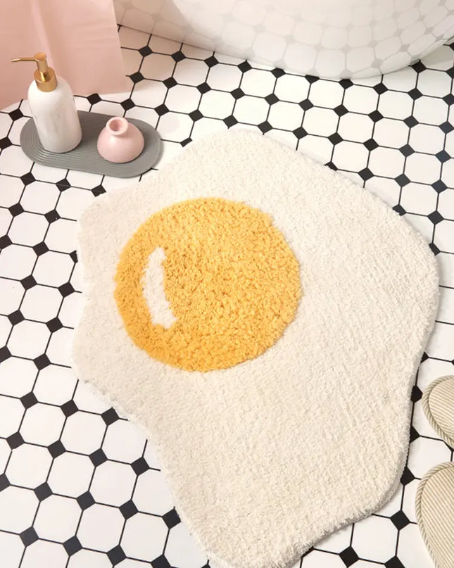 Poached egg design bath mat on a black and white geometric patterned floor.