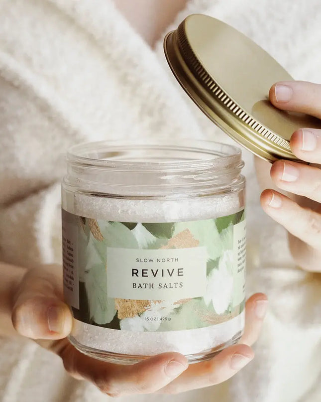 Hand holding Revive Bath Salts 15 oz glass jar with gold lid by Slow North