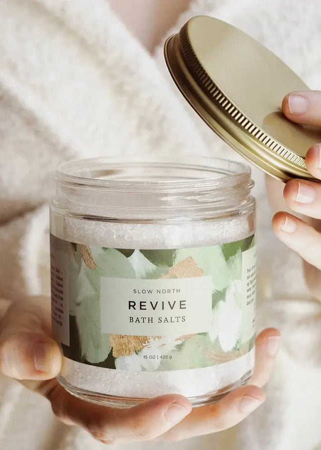 Hand holding Revive Bath Salts 15 oz glass jar with gold lid by Slow North