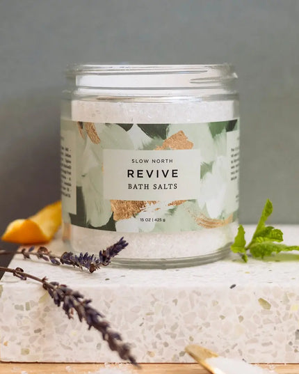 Jar of 'Revive' bath salts with a decorative label on a stone surface.