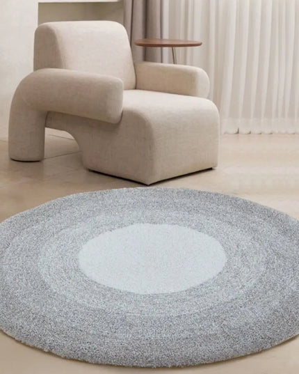 Round gray rug with a white center in front of a beige armchair.