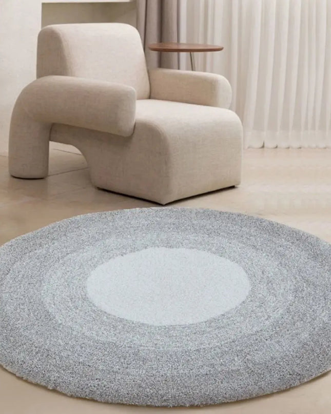Round gray rug with a white center in front of a beige armchair.
