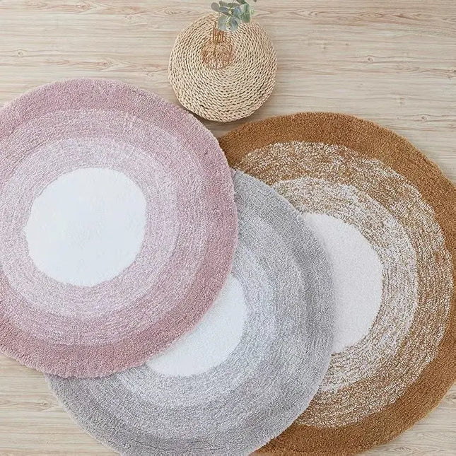 Three round rugs in pink, gray, and brown on a wooden floor.