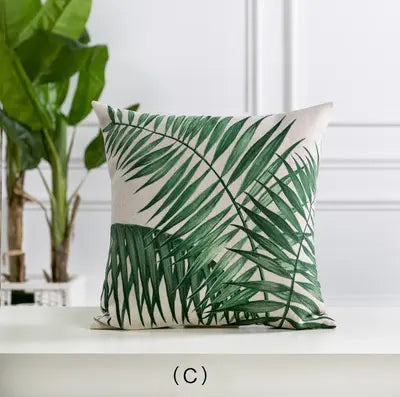 Pillow with green leaf pattern on a white surface with plants in the background