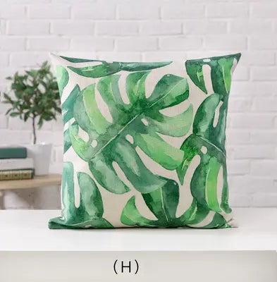 Green leaf-patterned pillow on a white surface with a white brick wall background