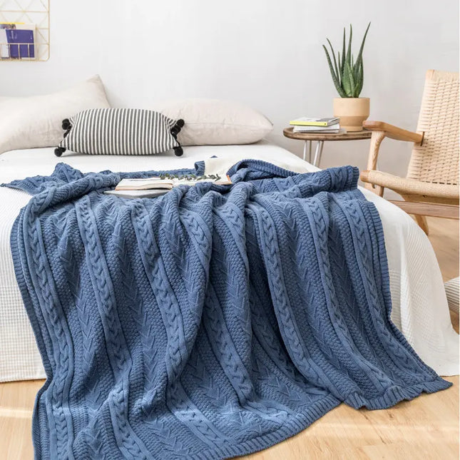 Blue knitted blanket draped over a bed in a cozy bedroom setting.