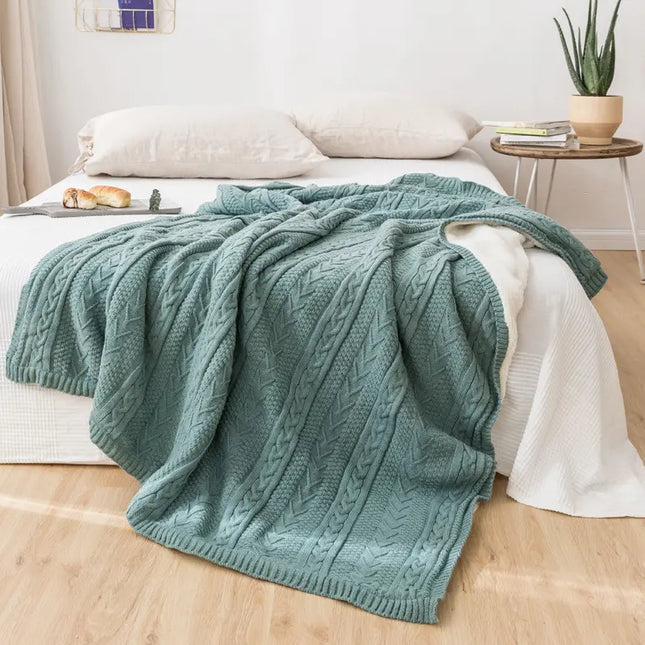 Green knitted blanket on a bed in a bedroom setting