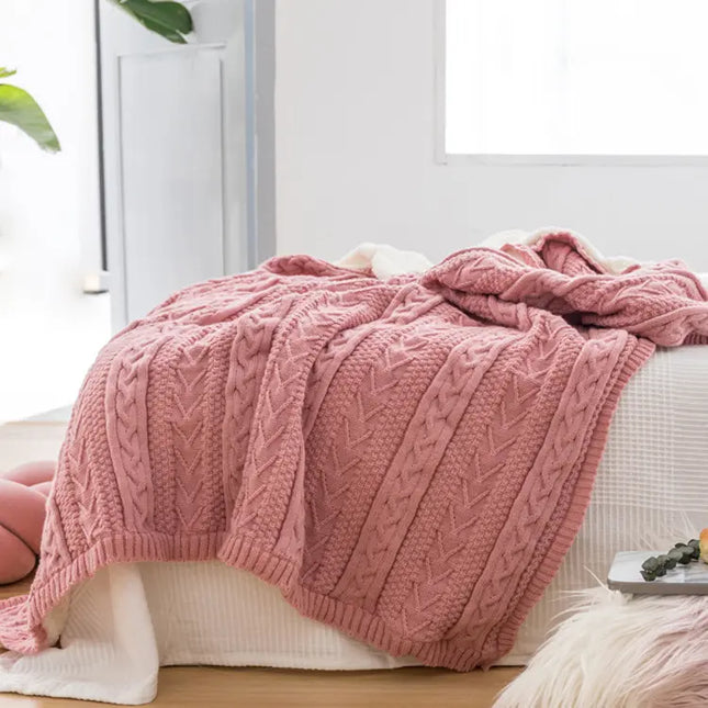 Pink knitted blanket draped over a white surface with a light background