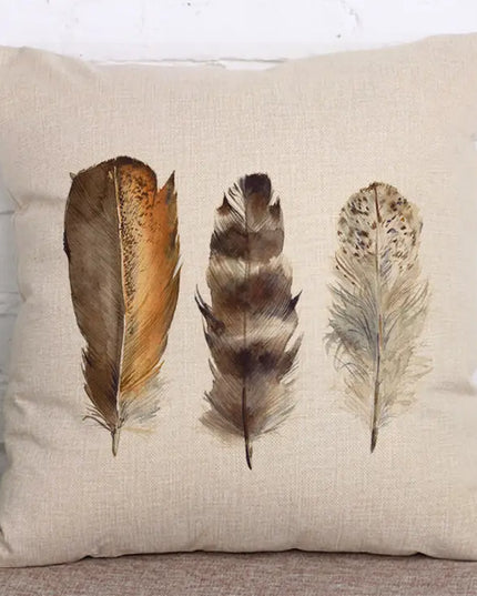 Decorative pillow with three feather illustrations on a textured surface.